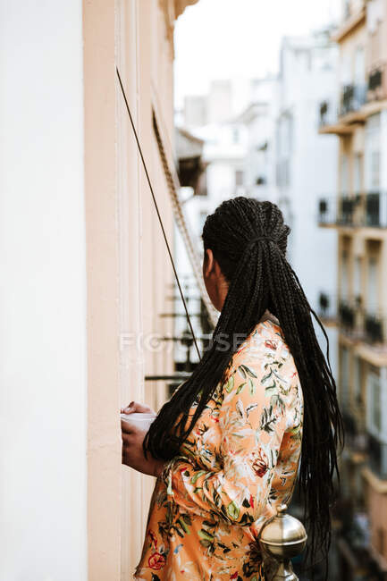 Giovane donna con tazza di caffè in piedi sul balcone — Foto stock