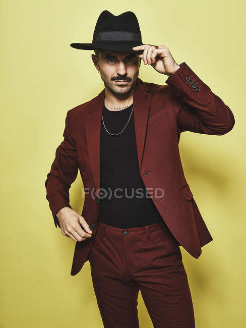 Bello barbuto ben vestito maschio in abito vinoso alla moda e cappello guardando la fotocamera sullo sfondo giallo — Foto stock