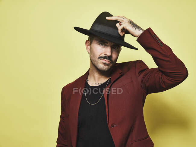 Handsome bearded well dressed male in trendy vinous suit and hat looking at camera against yellow background — Stock Photo