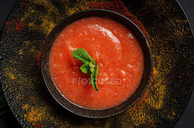 Sopa de tomate casera saludable con pan, menta y aceite de oliva sobre fondo oscuro desde arriba. Concepto de comida vegana - foto de stock