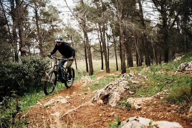 Homem de corpo inteiro no capacete andando de bicicleta no caminho pedregoso contra árvores durante a viagem pela floresta — Fotografia de Stock