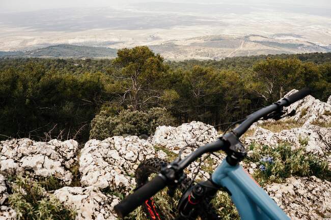 Modern bicycle placed on rough stony cliff near green forest during trip through nature — Stock Photo