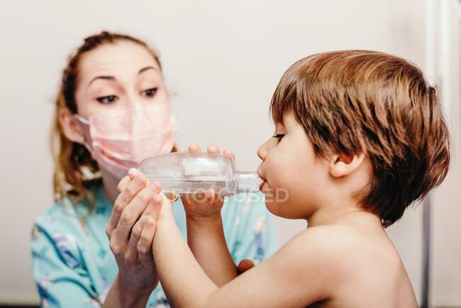 Niño pequeño que usa inhalador en la clínica durante el chequeo - foto de stock