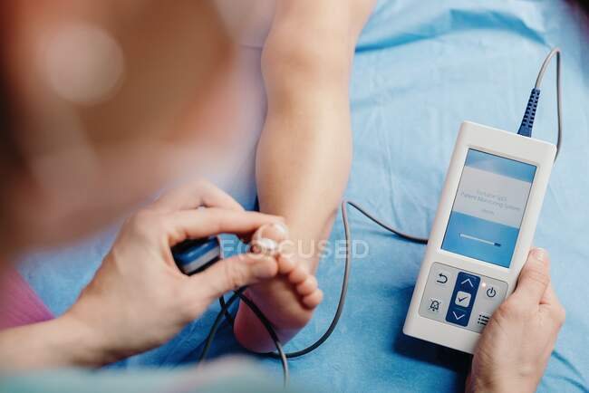 From above of crop medical specialist using pulse oximeter sensor while examining kid in hospital — Stock Photo