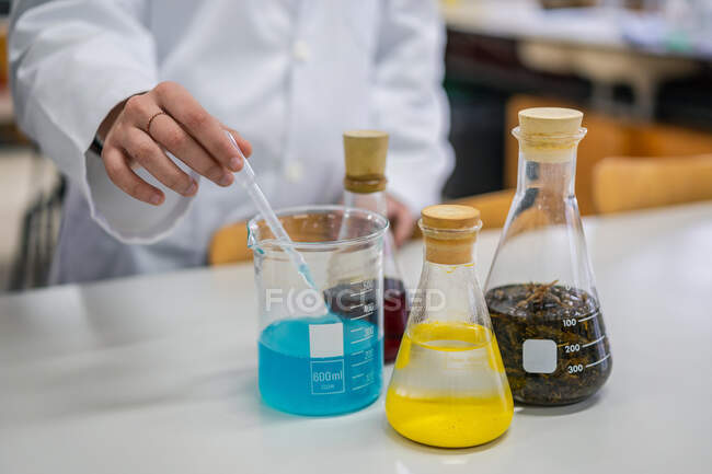 Químico irreconhecível tomando fluido azul com pipeta durante a realização de experimentos em laboratório moderno — Fotografia de Stock