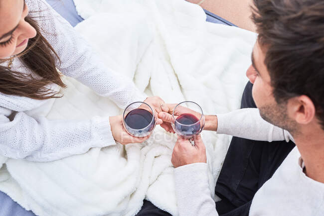 Von oben sieht man ein fröhliches junges Paar in Freizeitkleidung, das mit einem Glas Rotwein anstößt und gleichzeitig glückliche Momente miteinander genießt — Stockfoto