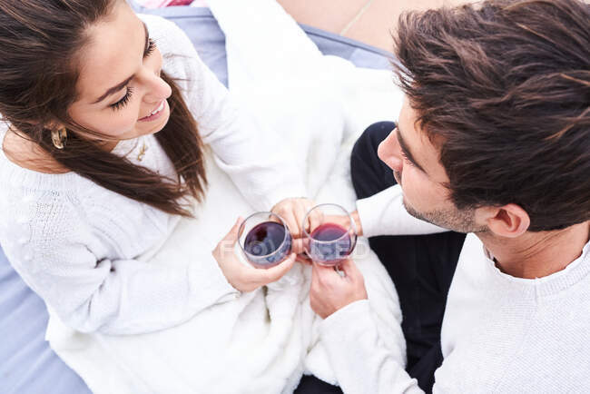 From above side view of cheerful young couple in casual wear toasting with glasses of red wine while enjoying happy moments together — Stock Photo