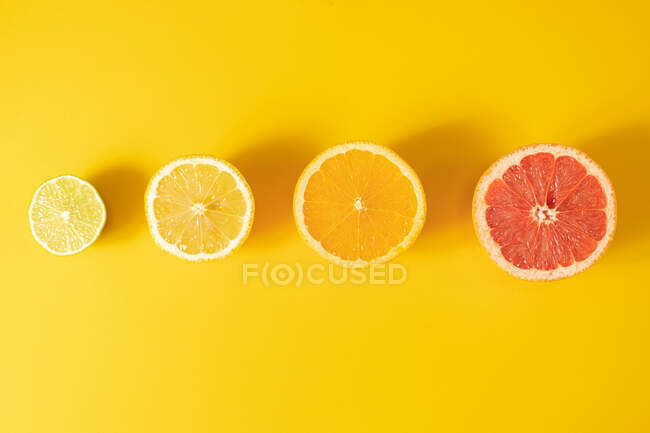 Draufsicht der Hälften verschiedener reifer Zitrusfrüchte, die in einer Linie auf gelbem Hintergrund angeordnet sind — Stockfoto