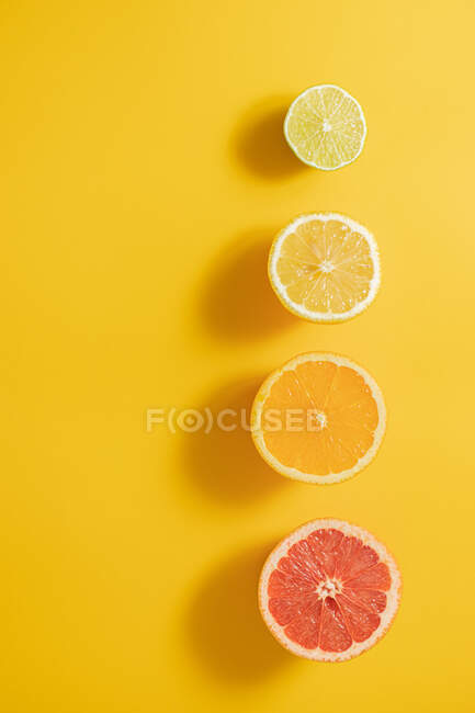 Vista superior de metades de citrinos maduros sortidos dispostos em linha sobre um fundo de superfície amarelo — Fotografia de Stock