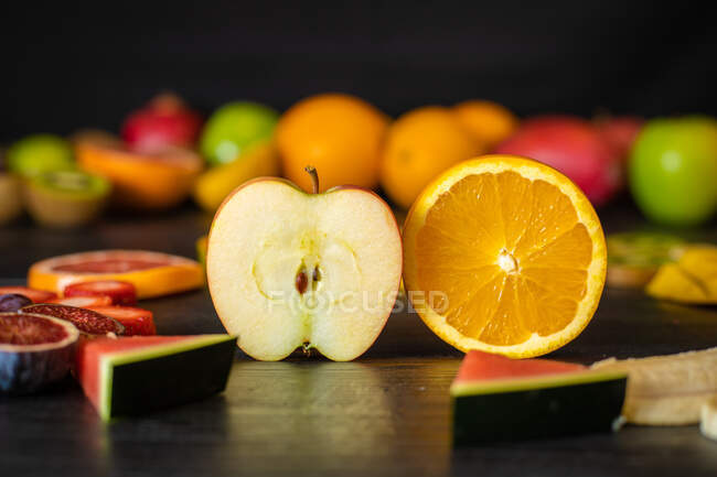 Различные очищенные и обрезанные здоровые фрукты и овощи расположены на черном столе пиломатериалов — стоковое фото