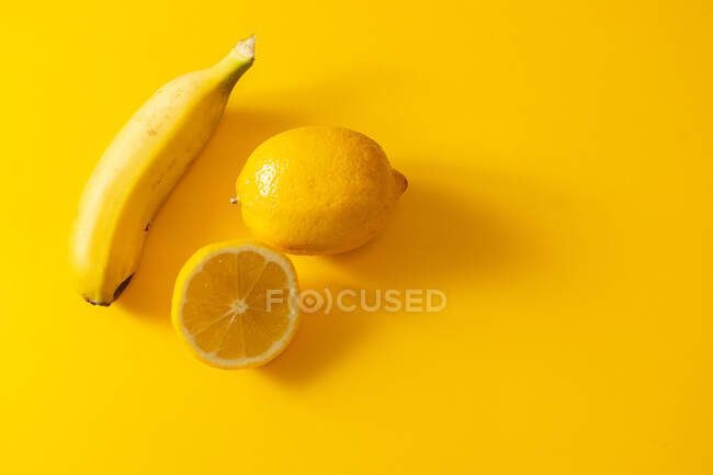 Зверху стиглий банан і свіжий лимон розміщені один біля одного на яскраво-жовтому тлі — стокове фото