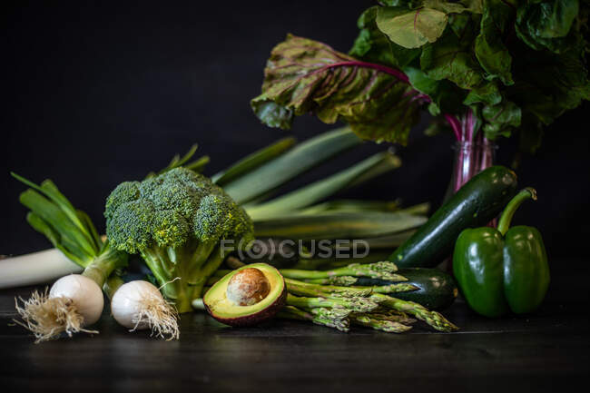 Група різних зелених овочів, розміщених на темному дерев'яному столі на чорному фоні — стокове фото