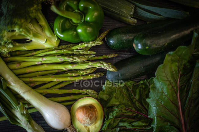 Mazzo di varie verdure verdi poste su tavolo di legno scuro su sfondo nero — Foto stock