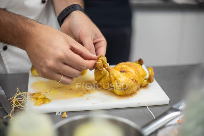 Cocinero irreconocible atando patas de codorniz marinada cruda mientras prepara delicioso plato en la cocina del restaurante - foto de stock