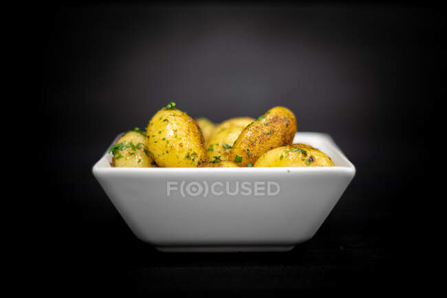 Square bowl of yummy roasted potatoes with herbs placed on black timber table — Stock Photo