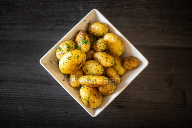 Von oben quadratische Schüssel mit leckeren Bratkartoffeln mit Kräutern auf schwarzem Holztisch — Stockfoto