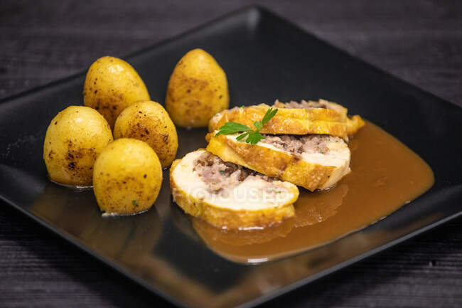 Кусочки вкусного фаршированного мясного рулета подаются с соусом и жареной картошкой на квадратной тарелке в кафе — стоковое фото