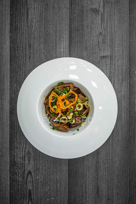 Vista superior da deliciosa carne frita servida com molho e ervas na placa de cerâmica na mesa de madeira preta — Fotografia de Stock