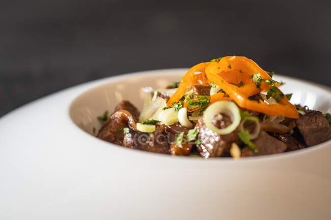 Жареное мясо подается с соусом и травами на керамической тарелке на черном деревянном столе — стоковое фото