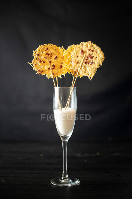 Glass with rice for decoration of crispy grated cheese chips on sticks placed on black background — Stock Photo