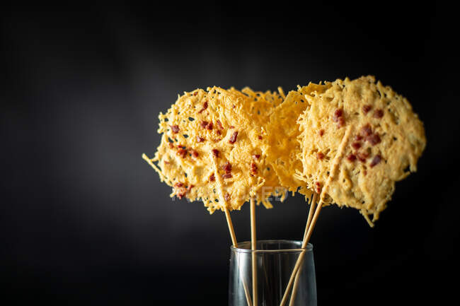 Vidro com arroz para decoração de batatas fritas de queijo ralado crocante em paus colocados no fundo preto — Fotografia de Stock