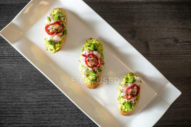 From above top view of delicious small sandwiches with shrimp and vegetables placed on ceramic plate on black table in cafe — Stock Photo