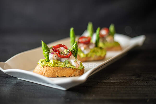 Closeup deliciosos pequenos sanduíches com camarão e legumes colocados em placa de cerâmica na mesa preta no café — Fotografia de Stock