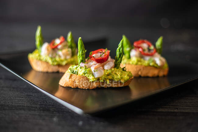 Closeup deliciosos pequenos sanduíches com camarão e legumes colocados em placa de cerâmica na mesa preta no café no fundo preto — Fotografia de Stock