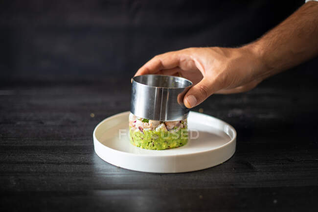 Кулінарний шеф-кухар з використанням металевого кільця, щоб сформувати смачний здоровий салат на керамічній тарілці на чорному столі в ресторані — стокове фото