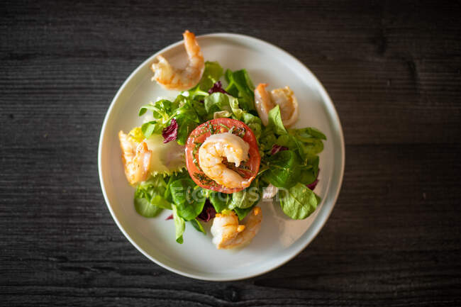 Vista dall'alto di sana insalata di spinaci con gamberetti e pomodoro servita su piatto di ceramica withe sul tavolo nero — Foto stock