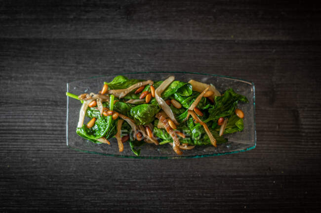 Сверху стеклянная тарелка вкусного салата со шпинатом с грибами, размещенная на черном деревянном столе в кафе — стоковое фото