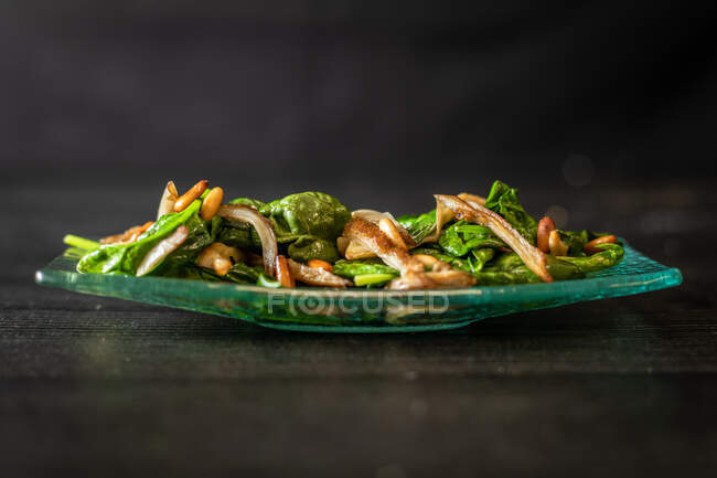 From above glass plate of tasty spinach salad with mushrooms placed on black wooden table in cafe — Stock Photo
