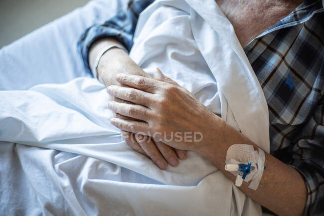 Зверху пацієнт похилого віку з внутрішньовенним катететером в руці лежить під ковдрою і спить — стокове фото