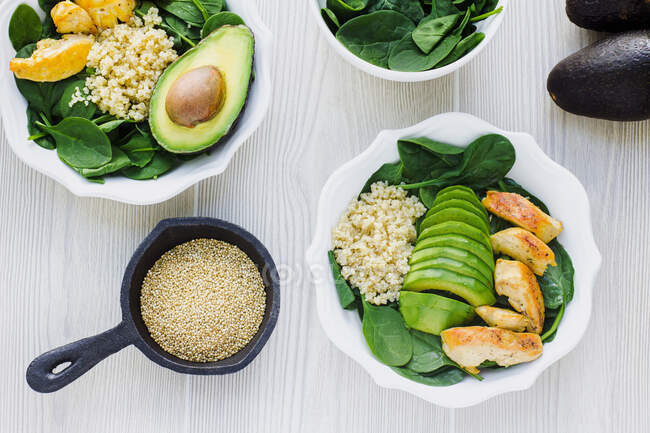 Top view of white bowls with green spinach garnished with couscous and avocado with friend chicken on wooden table — Stock Photo