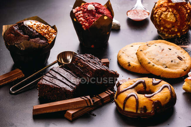 Various doughnuts with sweet toppings and chocolate bars composed with cup of cappuccino on black table — Stock Photo