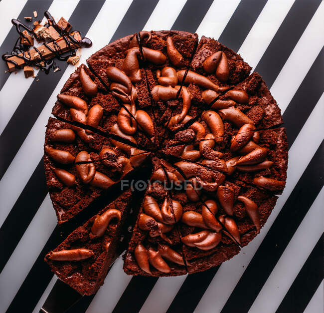 Overhead-Ansicht von ganzen süßen Schokoladenkuchen mit Schokoriegel auf gestreifter schwarz-weißer Oberfläche — Stockfoto