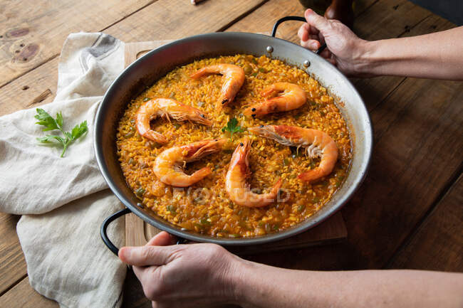 Hands holding metal pan of paella with roasted shrimps — Stock Photo