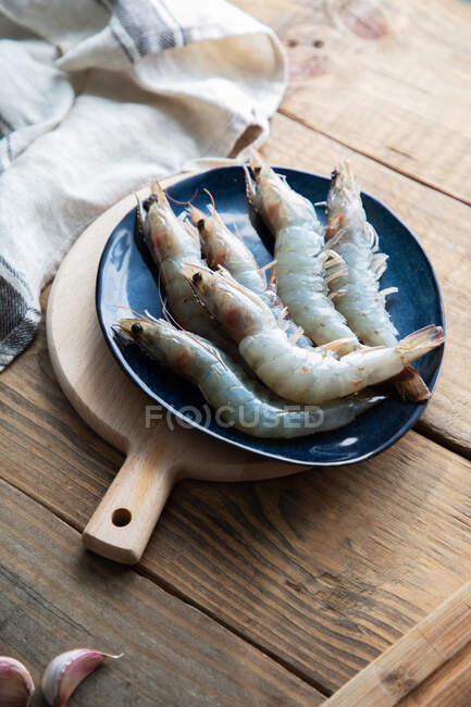 Grosses crevettes grises crues sur grande plaque bleue sur planche à découper — Photo de stock