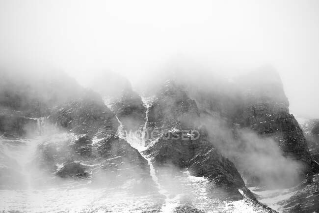 Nuvole spesse che galleggiano sulle cime delle montagne innevate nelle maestose Dolomiti, in bianco e nero — Foto stock