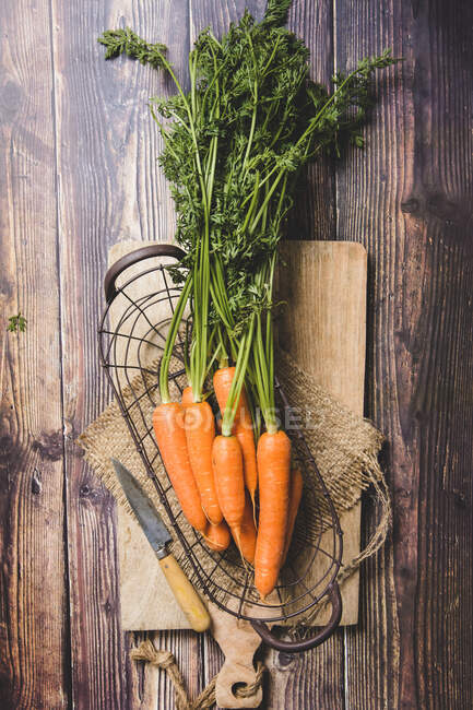 Верхний вид собранной спелой моркови с зеленой листвой, помещенной на раскройную доску на деревянном столе — стоковое фото