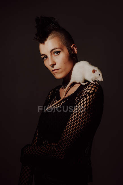 Confident woman with mohawk carrying white rat on shoulder and looking at camera against black background — Stock Photo