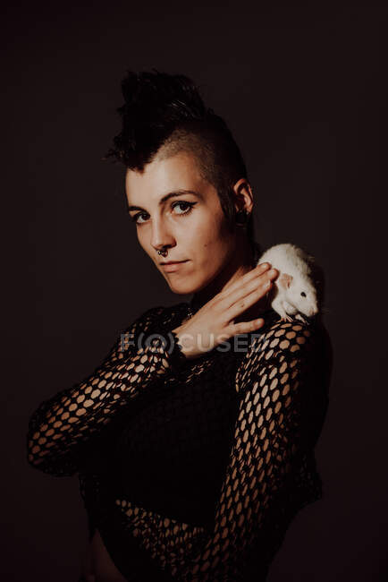 Confident woman with mohawk carrying white rat on shoulder and looking at camera against black background — Stock Photo