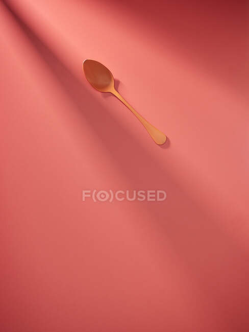 Cucchiaio di plastica arancione su sfondo corallo alla luce del sole — Foto stock