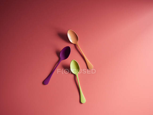 Cucchiai colorati su sfondo di carta rossa — Foto stock