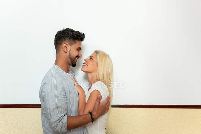 Positivo uomo e donna diversi abbracciarsi e guardarsi mentre in piedi contro il muro — Foto stock