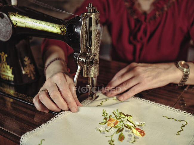 Старша леді в окулярах використовує ретро швейну машинку для створення лляної серветки в затишній кімнаті вдома — стокове фото