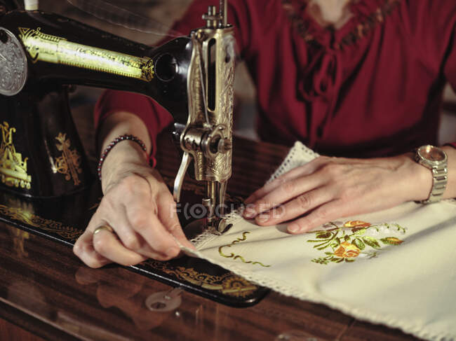 Senior signora in bicchieri utilizzando macchina da cucire retrò per creare tovagliolo di lino in camera accogliente a casa — Foto stock