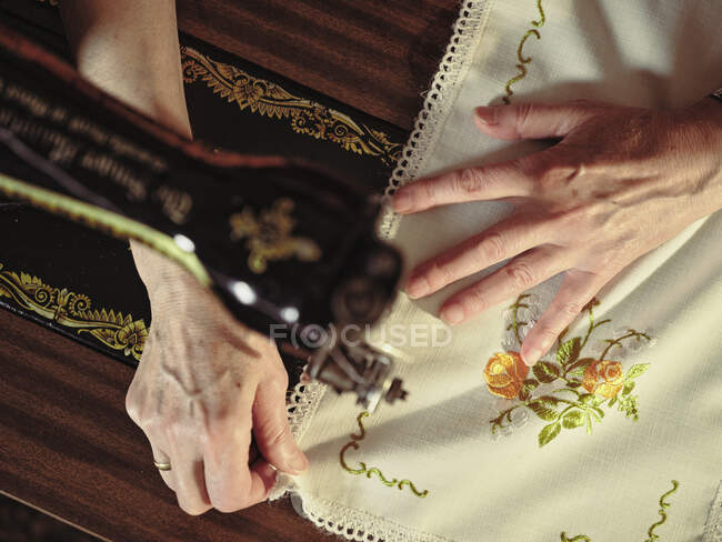 Senior dame dans les lunettes en utilisant une machine à coudre rétro pour créer une serviette de lin dans une chambre confortable à la maison — Photo de stock