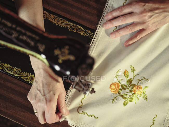 Senior senhora em óculos usando máquina de costura retro para criar guardanapo de linho no quarto acolhedor em casa — Fotografia de Stock