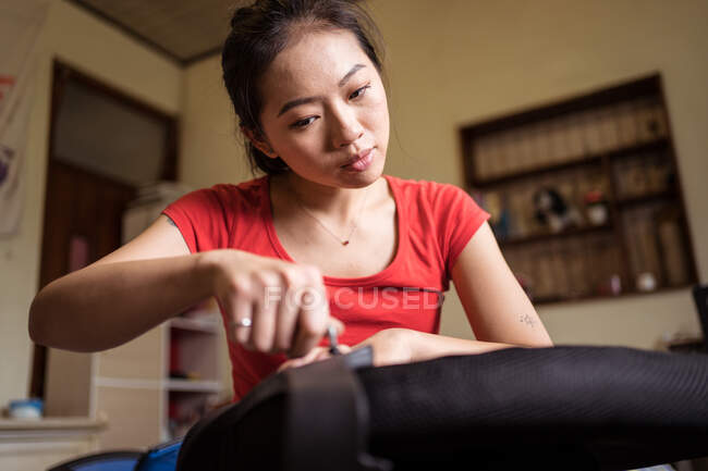 Giovane donna asiatica etnica con anello su mignolo girando le dita vite durante l'installazione di maniglia sulla sedia a casa — Foto stock